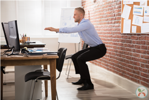 Man doing squats beside his desk.